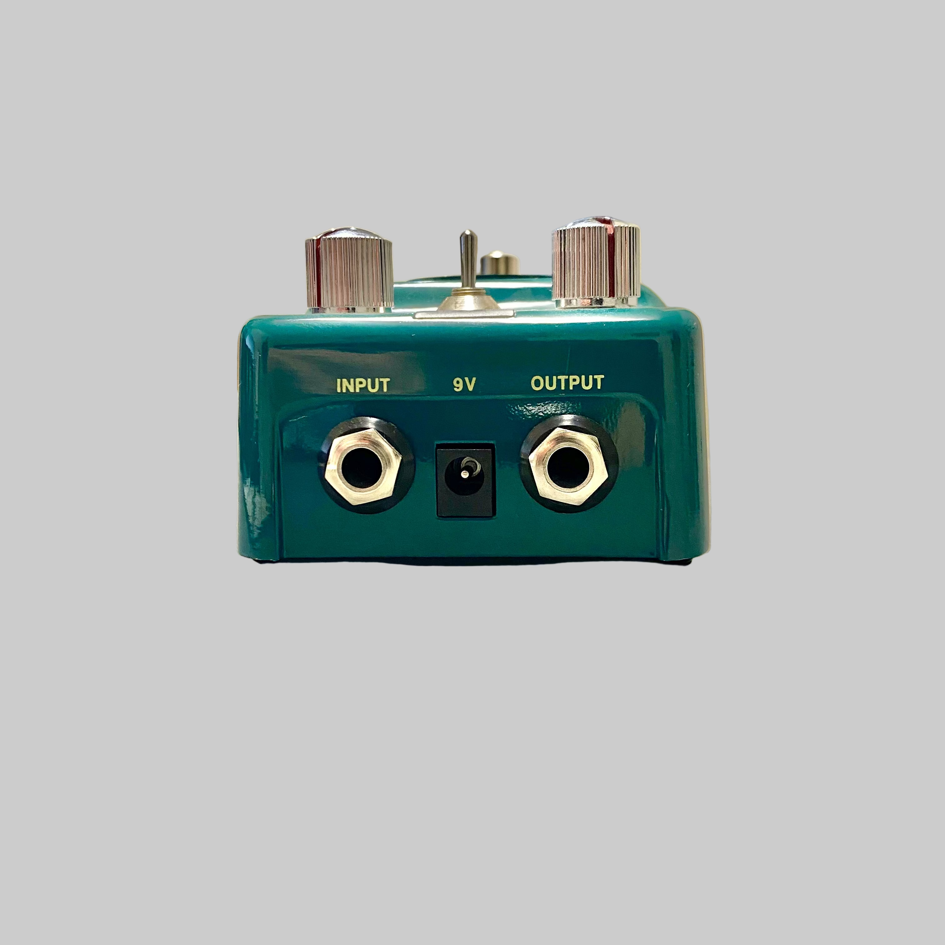 Green guitar effects pedal with input and output jacks on a reflective surface.
