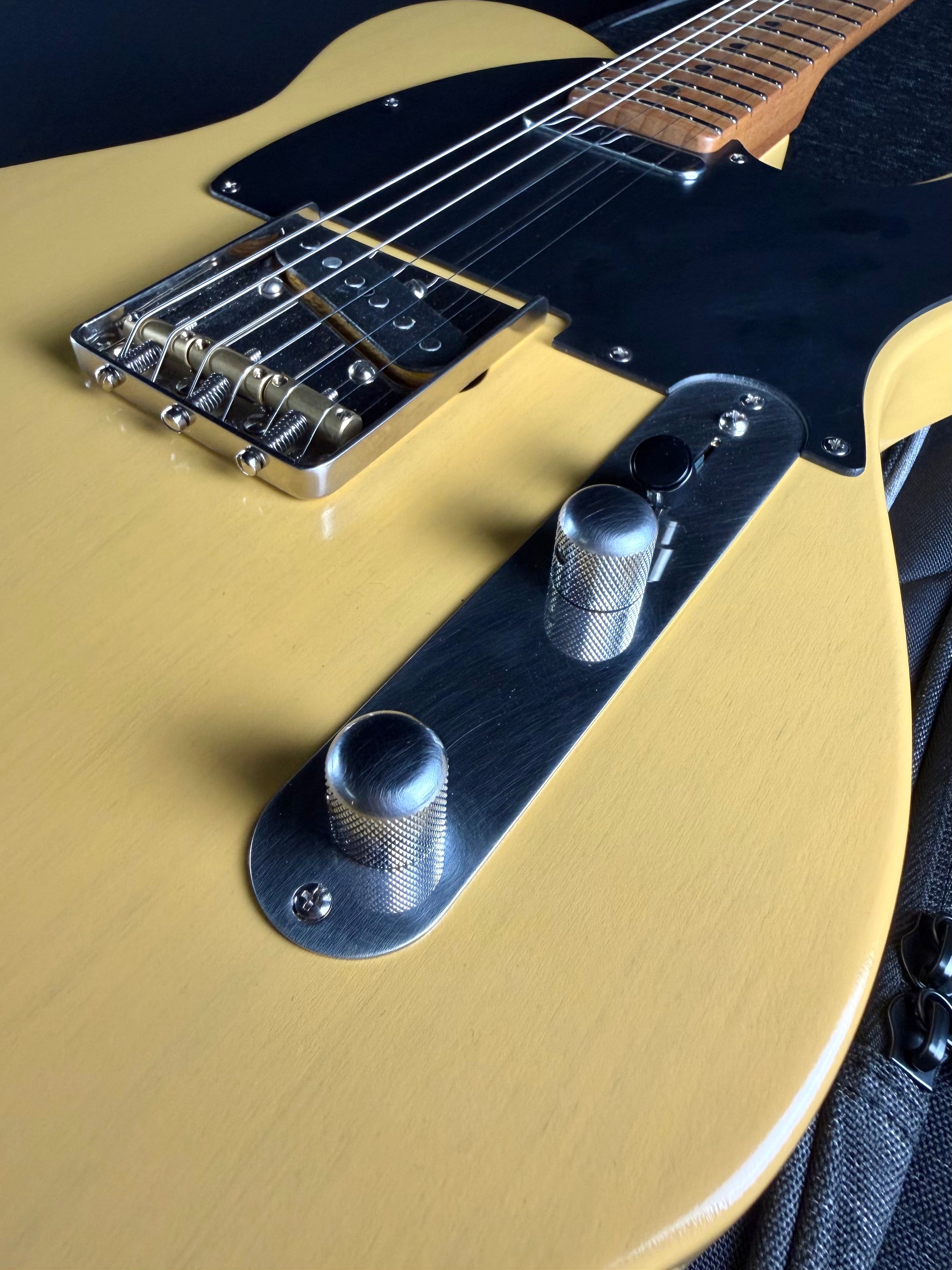 Close-up of a butterscotch-colored electric guitar with a black pickguard.