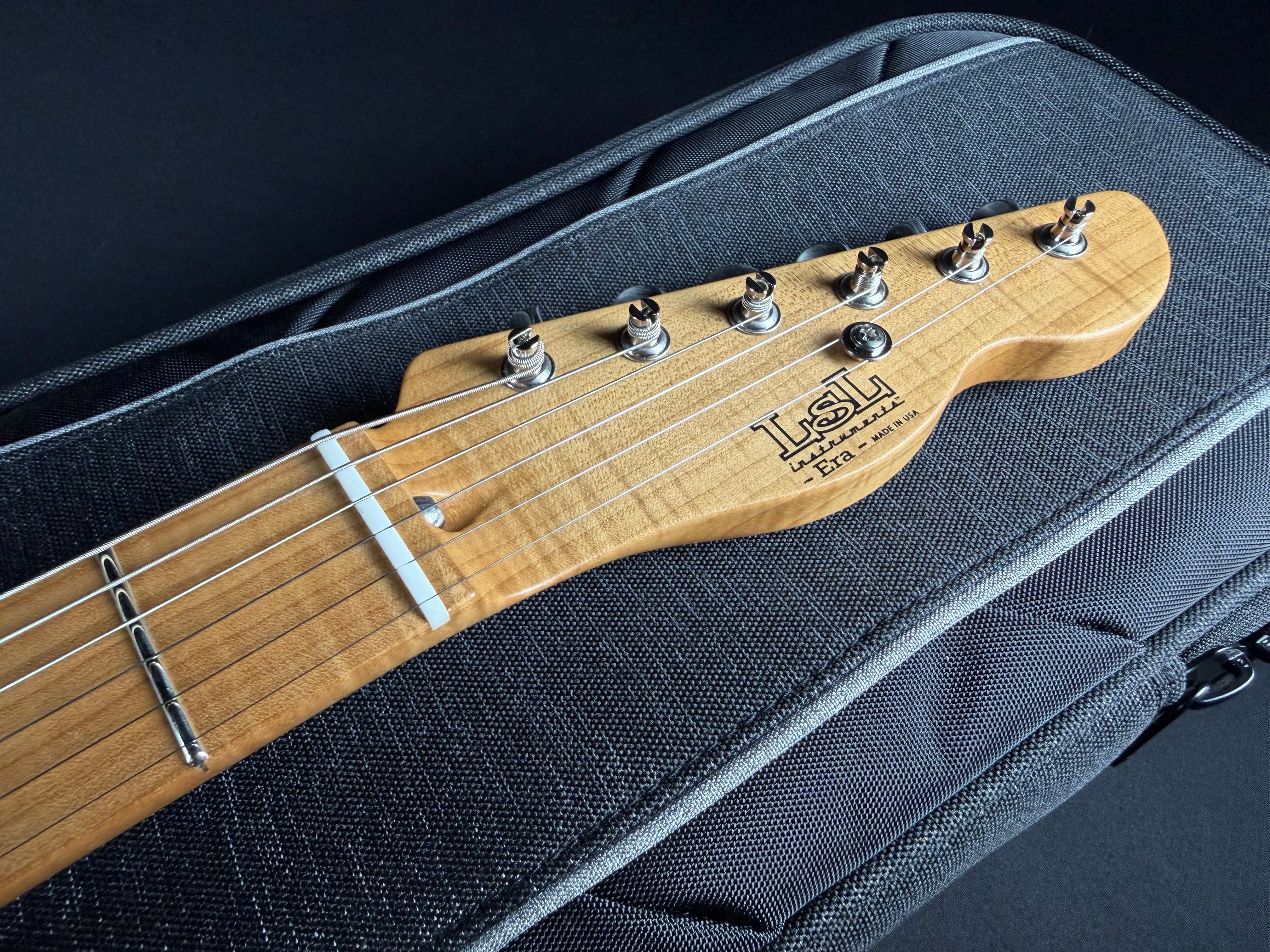 Guitar headstock with 'LSL' branding on a black guitar case.
