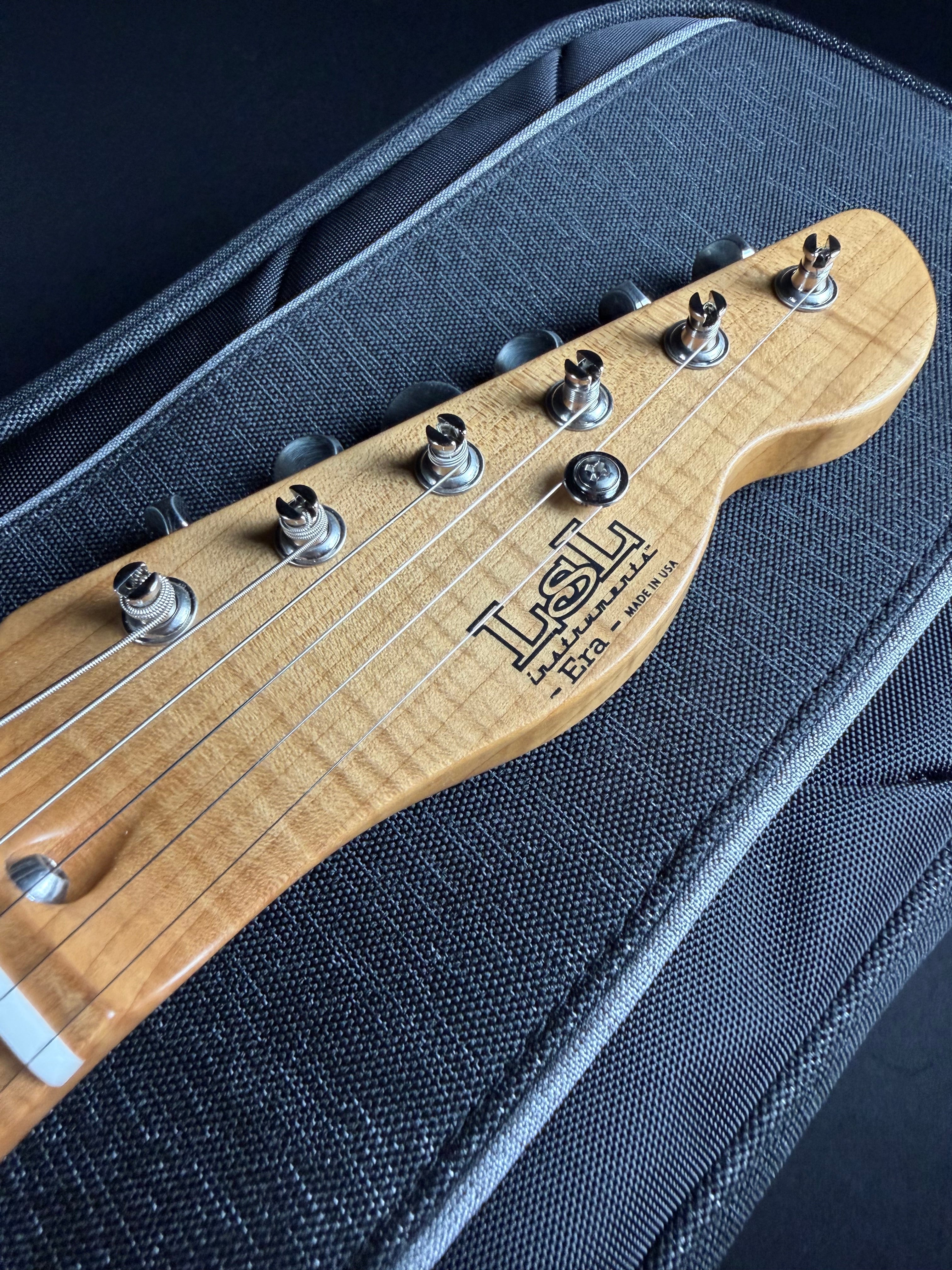 Close-up of a guitar headstock with 'LSL' branding on a textured black background