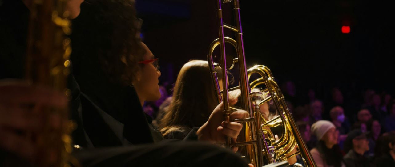 Person playing a brass instrument on stage with an audience in the background