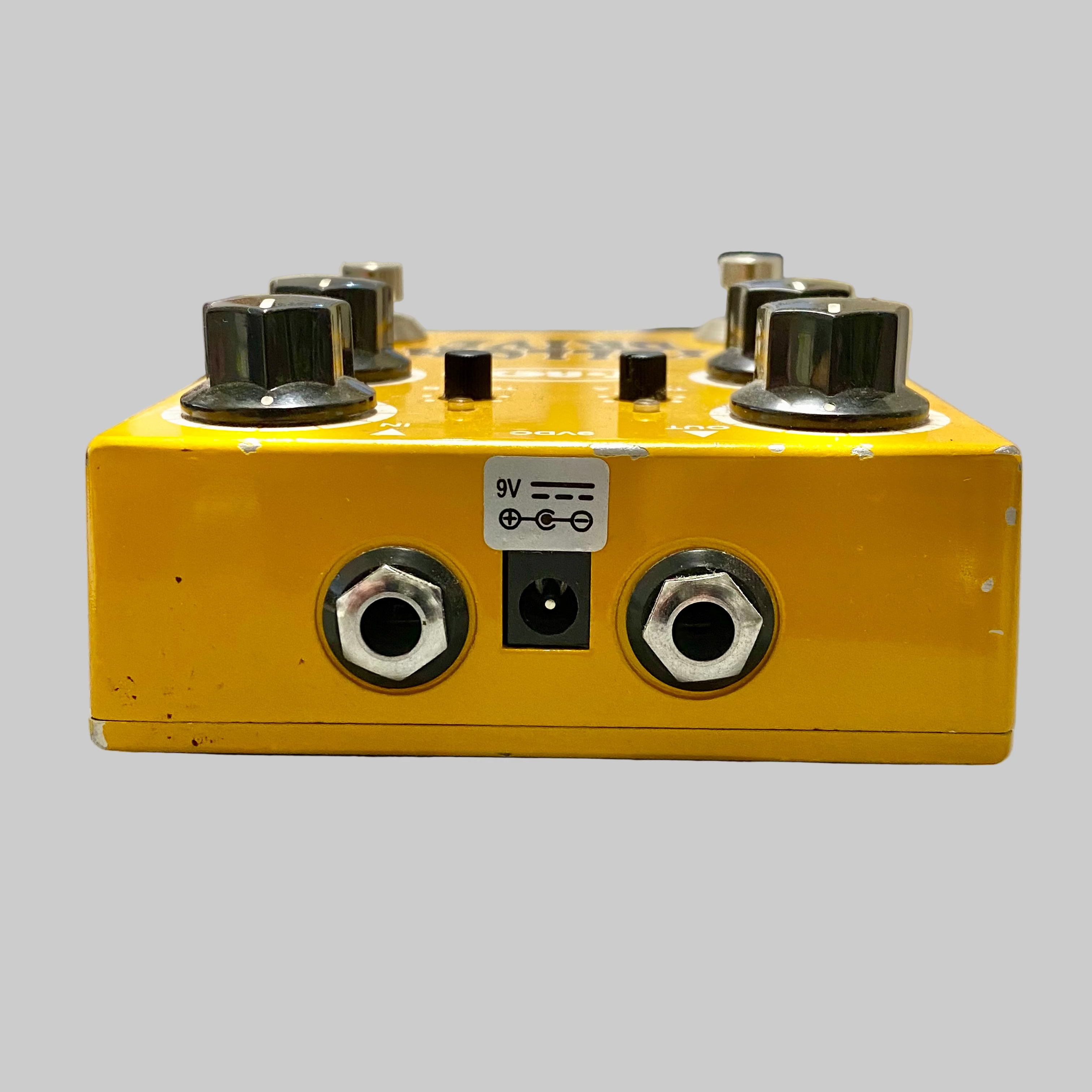 Yellow guitar effects pedal with knobs and jacks on a gray surface