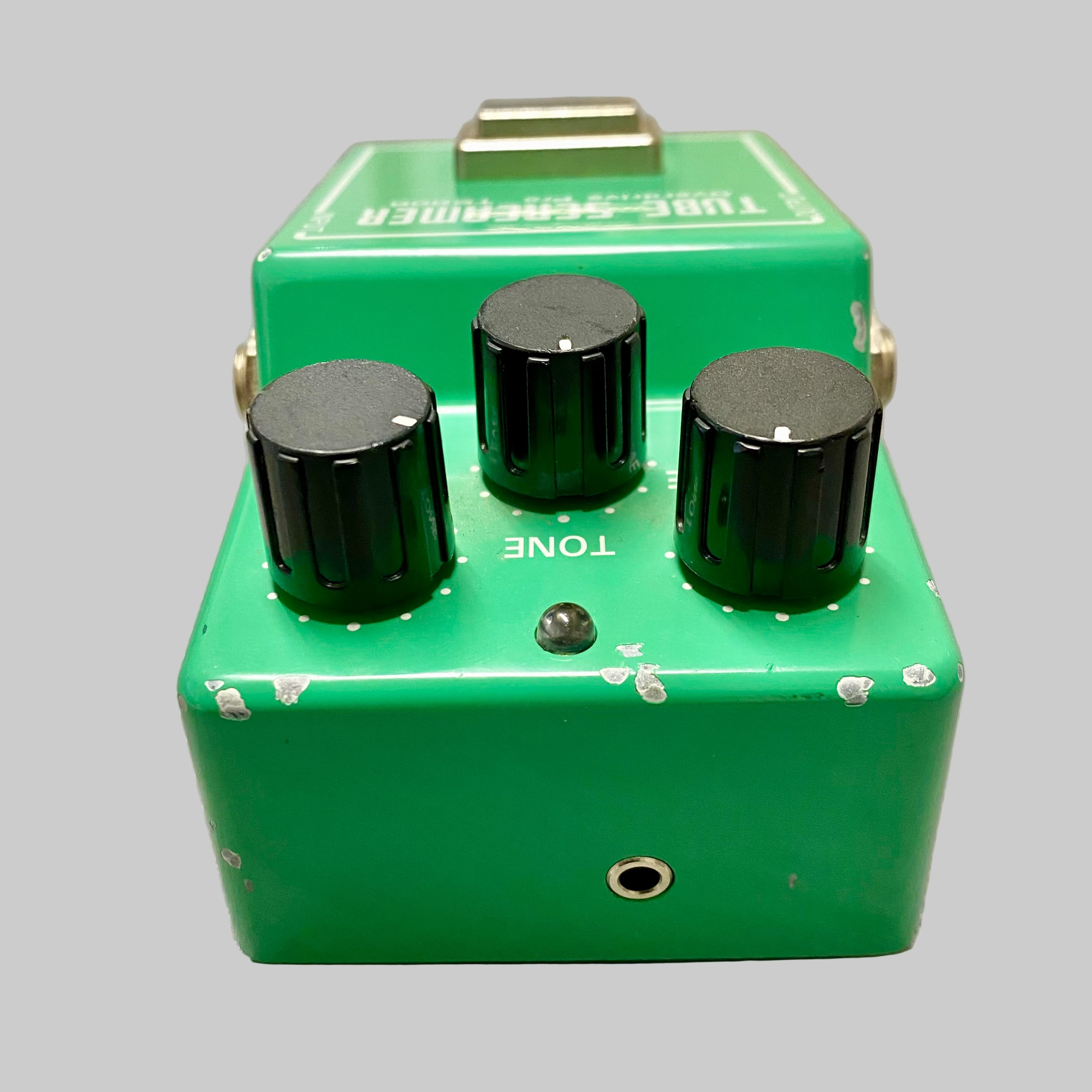 Green guitar effects pedal with three knobs on a gray surface
