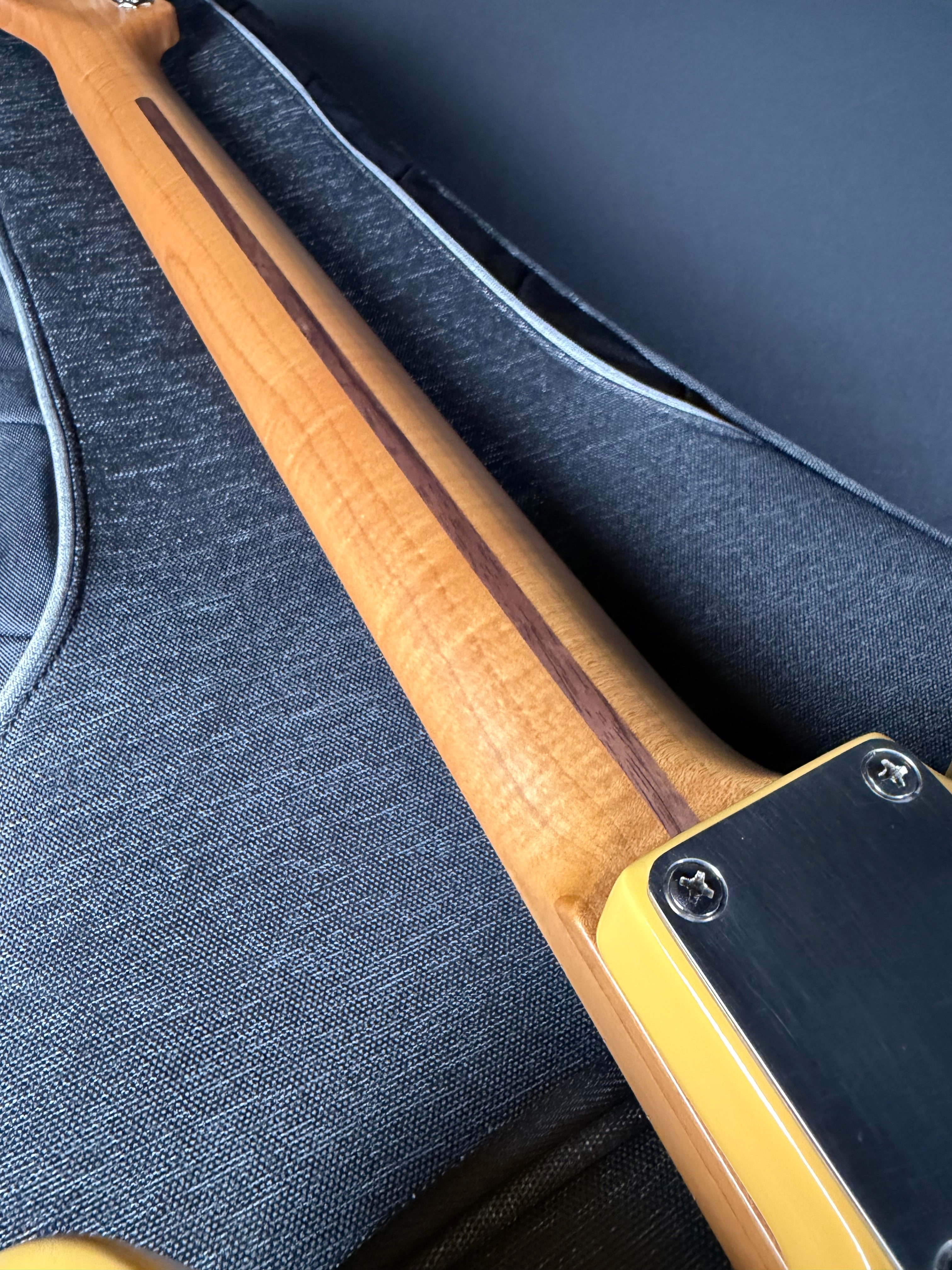 Close-up of a guitar neck with a wooden finish on a dark blue guitar case.