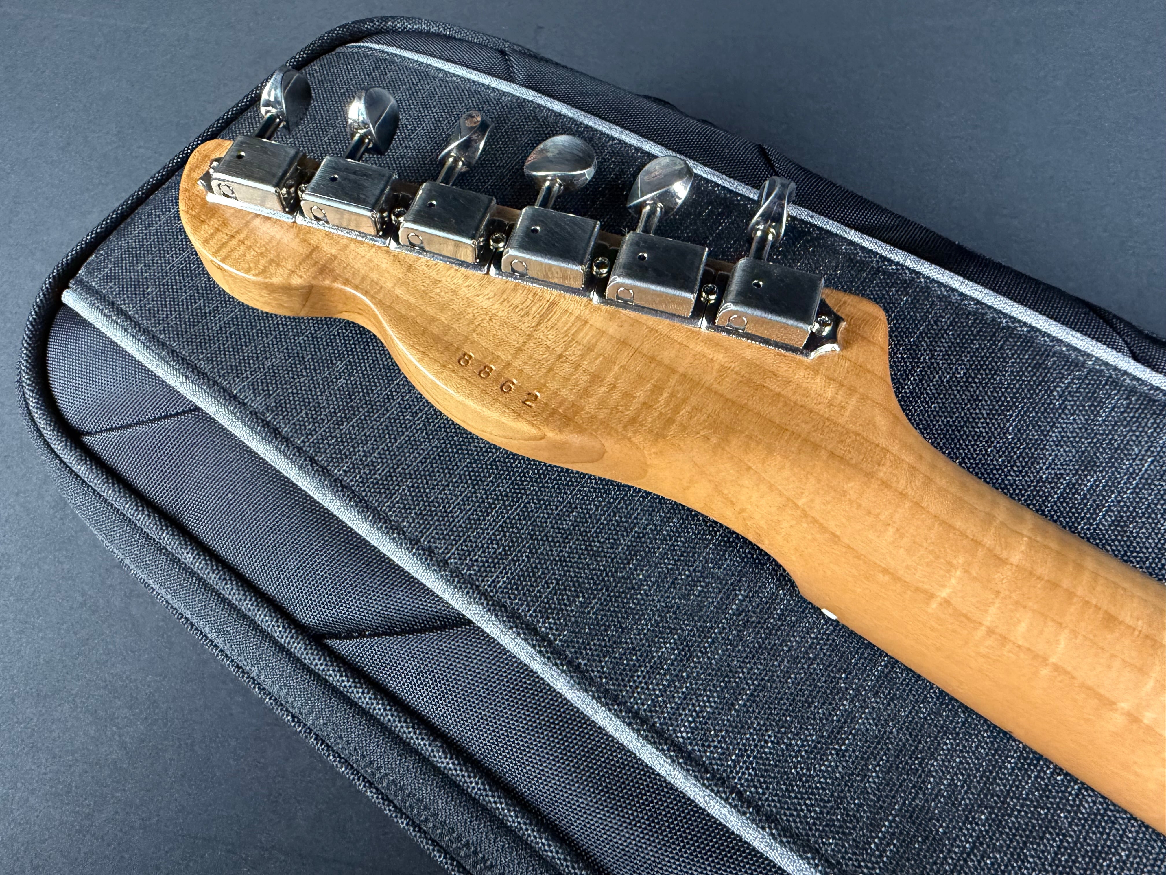 Close-up of a guitar's headstock with tuning pegs on a dark case.