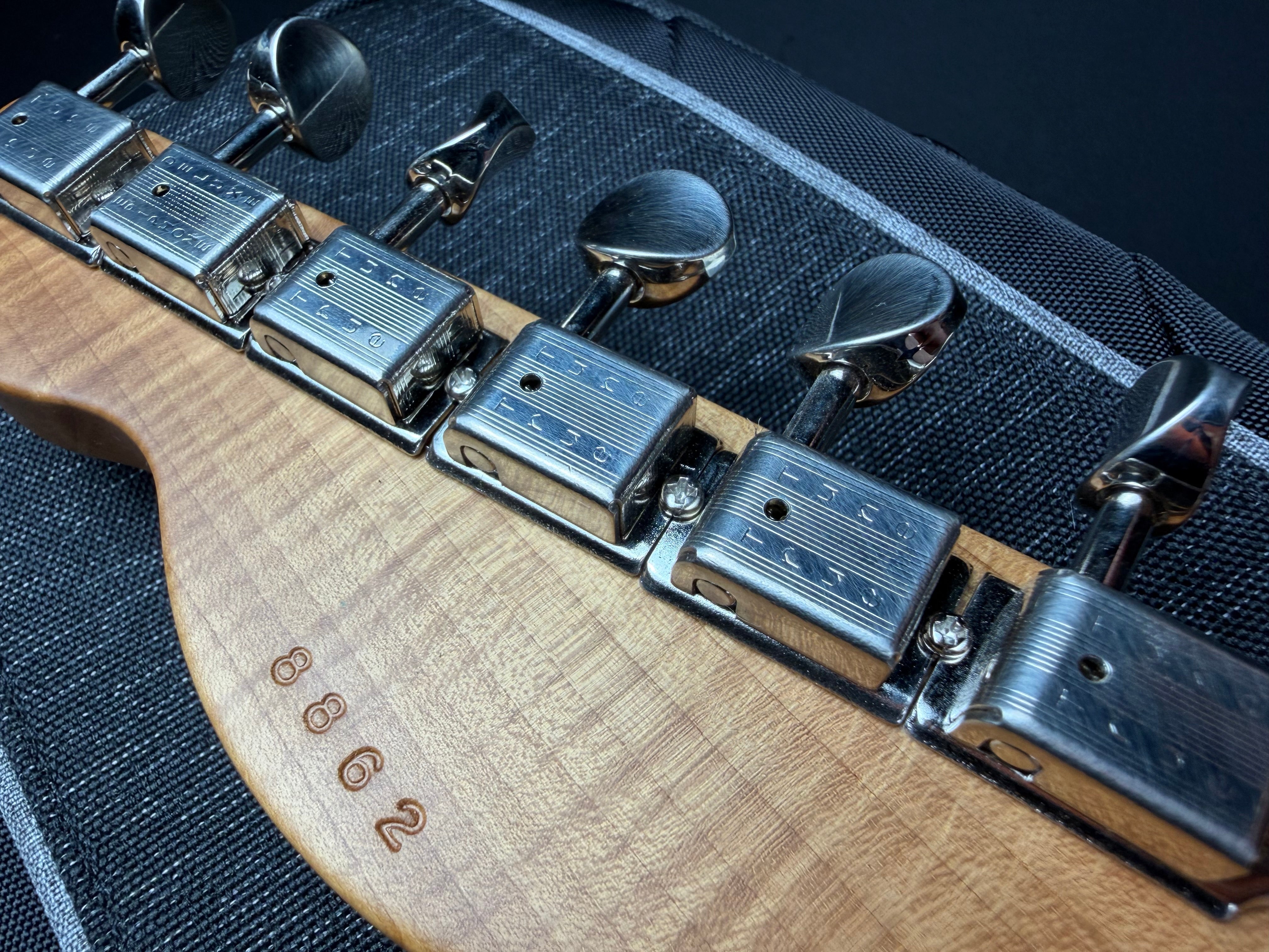 Close-up of a guitar's tuning pegs with a wooden neck and 'True Tune' branding.