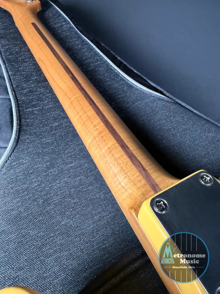 Close-up of a guitar neck with a wooden finish on a dark blue guitar case.