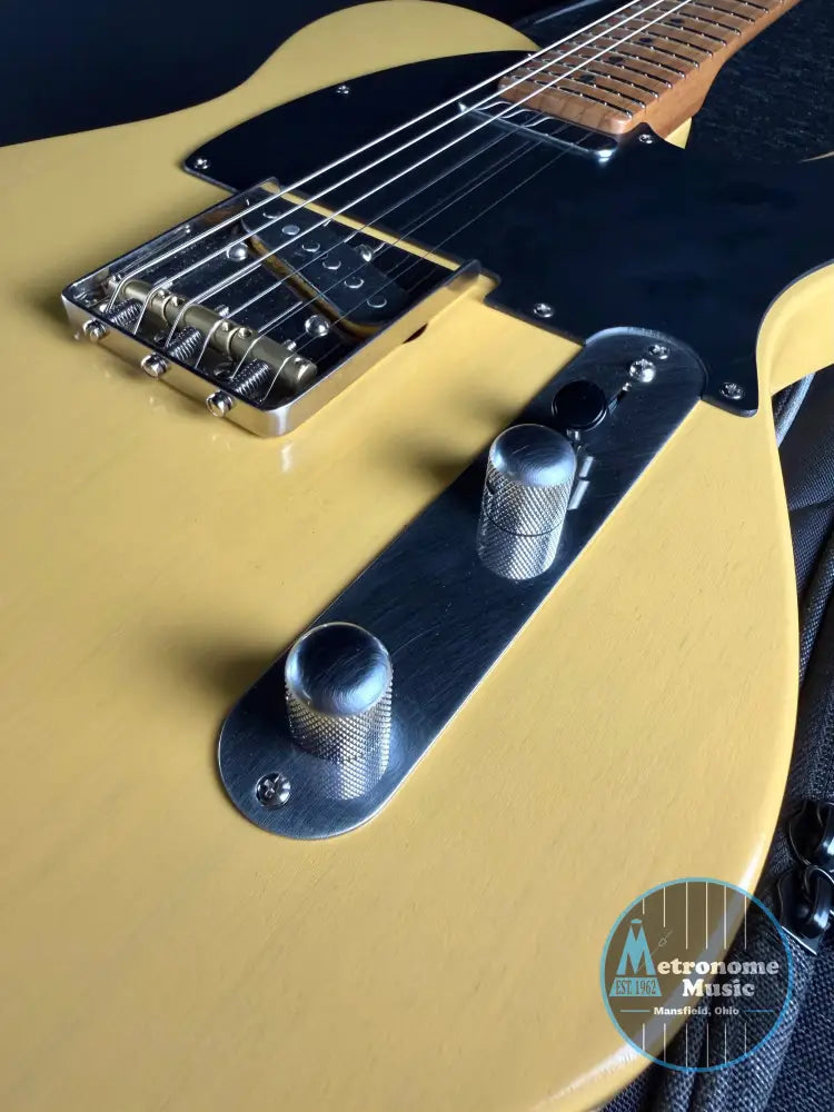 Close-up of a butterscotch-colored electric guitar with a black pickguard.